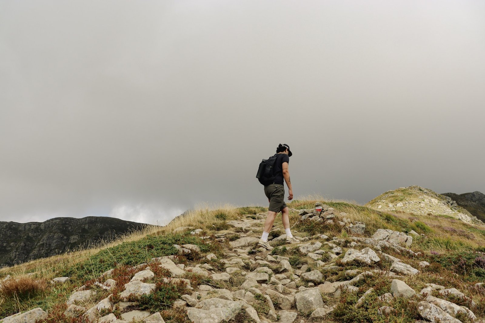 Escursionista su un sentiero roccioso in montagna sotto un cielo coperto